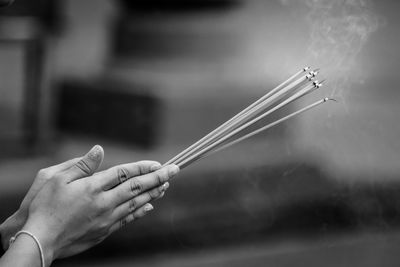 Cropped hands of woman holding burning incense sticks while praying outdoors