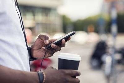 Midsection of man using phone while holding coffee cup in city