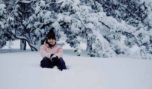 Woman sitting on snow covered land and tree
