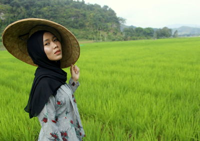 Portrait of woman in asian style conical hat standing on field