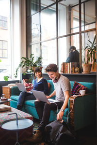 Smiling female professional talking with male colleague sitting on sofa at office