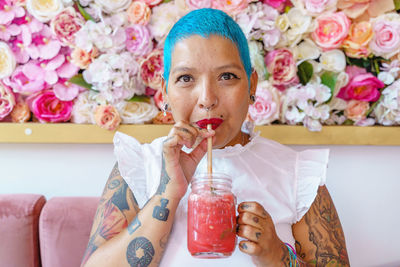 Soft focus of glad female with dyed hair and tattoos sitting in cafe drinking glass jar of fresh nonalcoholic beverage with straw