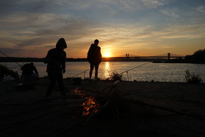 Silhouette people on beach against sky during sunset