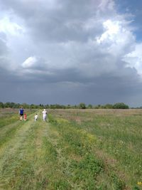 Rear view of family walking on grassy field against cloudy sky