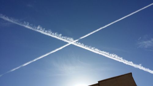 Low angle view of vapor trails against blue sky