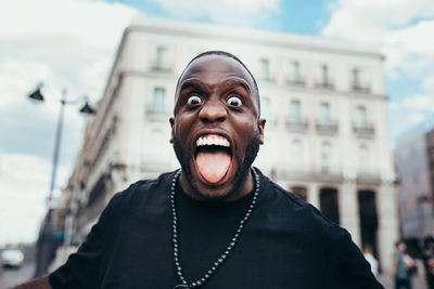 Portrait of cheerful black in urban scenery sticking out tongue and looking at camera