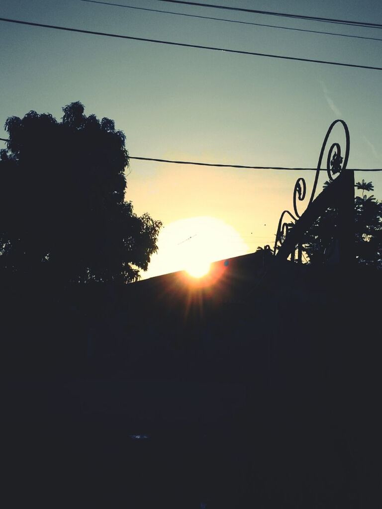 sunset, sun, silhouette, tree, sky, sunlight, clear sky, power line, sunbeam, built structure, lens flare, nature, outdoors, low angle view, electricity pylon, architecture, no people, transportation, orange color, building exterior