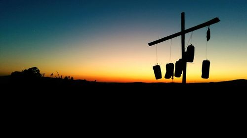 Silhouette signs hanging on cross against sky during sunset