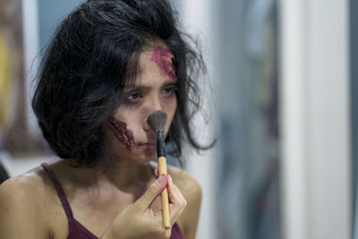 Close-up of woman applying make-up on face during halloween