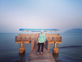 Woman standing on pier over sea against clear sky