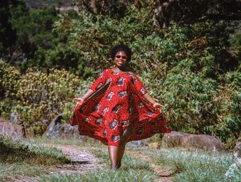 Woman walking while holding red dress on grass