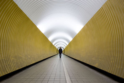 Rear view of man walking in illuminated tunnel