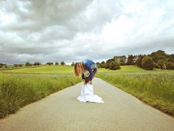 Woman wearing skirt on road amidst grassy field against sky