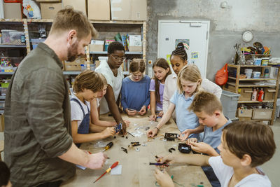 Group of male and female students working on robotics project with teachers in technology workshop in school