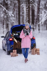 A woman in a winter snow-covered forest in the trunk of a car decorated with christmas decor.