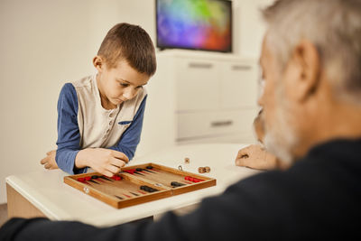 Concentrated boy playing backgammon with grandfather at home