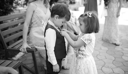 Cute sister adjusting brother tie with people in background during wedding