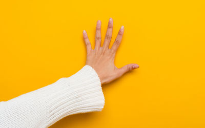 Hands of a beautiful woman with clean long nails on a yellow background