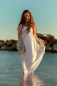 Portrait of beautiful woman standing in sea against sky