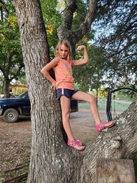 Portrait of girl flexing muscle while standing on tree trunk at park