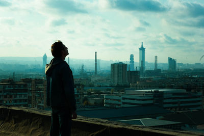 Rear view of man looking at cityscape against sky