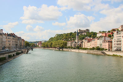 River passing through city buildings against cloudy sky