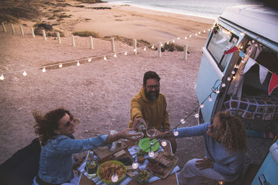 Male and female friends toasting while sitting by motor home during sunset