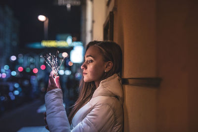 Young woman holding illuminated string light at night