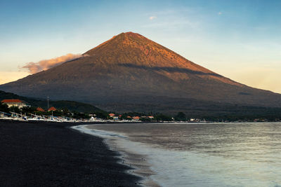 Sunrise at the black sand beach coast of amed, bali and mount agung volcano in the background