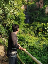 Side view of young man looking at trees in forest