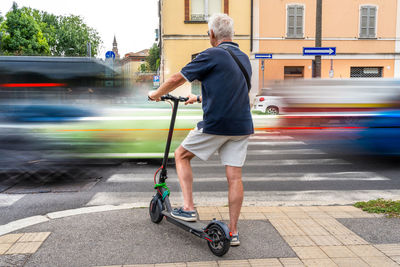 Commuter man using electric scooter is waiting to cross a road with heavy traffic. eco concept