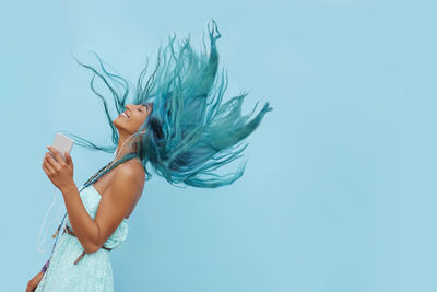 Cropped hand of woman holding flower against blue background