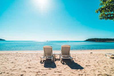 Deck chairs at beach against sky