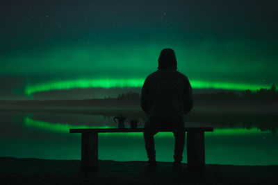 Rear view of man sitting on seat against sky at night