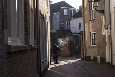 Rear view of man walking on footpath amidst buildings in city