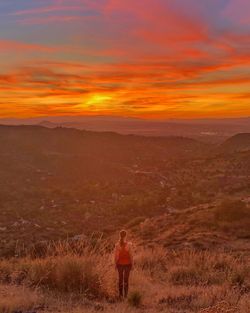 Rear view of man standing on land against sky during sunset