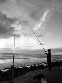 Man fishing in sea against sky