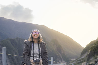 Happy woman carrying camera while standing against mountain during foggy weather