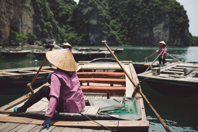 Rear view of woman wearing asian style conical hat while sitting on rowboat at halong bay