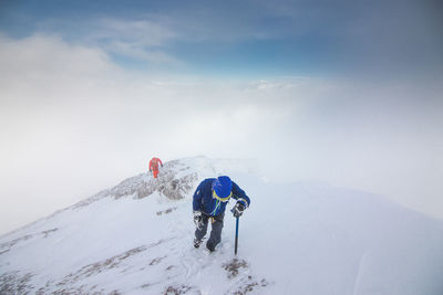 Hikers walking on snow covered mountains against sky