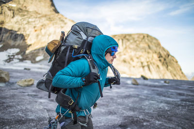 Mountaineer lifts heavy backpack onto shoulders while crossing glacier