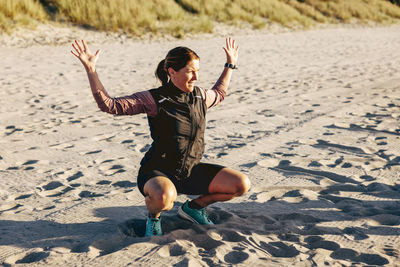 Mature female instructor explaining exercise posture while crouching on sand at beach