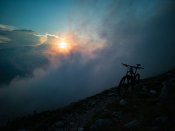 Silhouette of bicycle on rock against sky during sunset