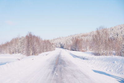 Road amidst bare trees on snow covered field against clear sky