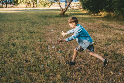 A boy is playing with soap bubbles in a summer park, among the greenery.