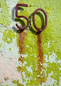 Rusty metallic number 50 on moss covered wall during sunny day