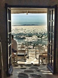 Rear view of man sitting on chair by sea