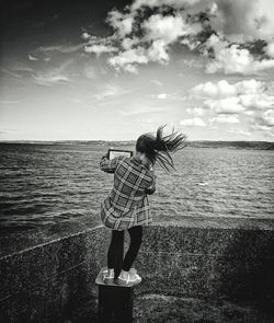 Rear view of girl with tousled hair looking at sea against sky