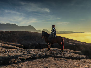 Rear view of man standing on mountain against sky during sunset