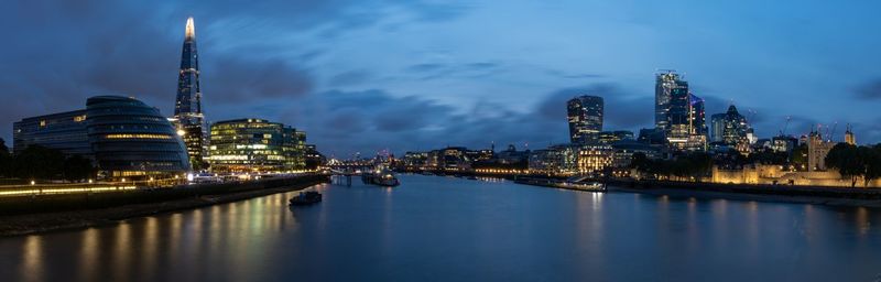 Illuminated buildings by river against sky at night